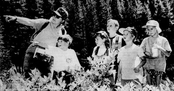 A guide points out berries to a group of children during a hike