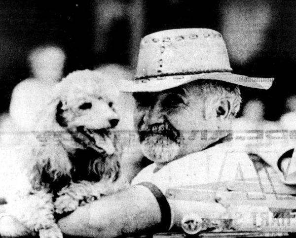 A man in a hat poses with his poodle