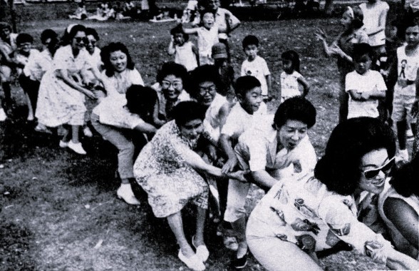 A large group of women and children play tug-of-war