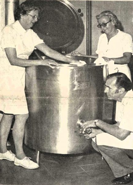 Three school cafeteria workers clean an industrial cook pot