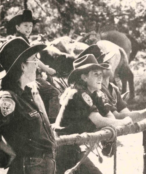 Two guides at a horseback riding camp lean on a fence