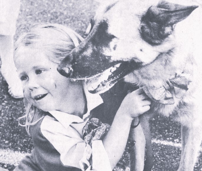 A little girl poses with her dog who is wearing a bow tie.