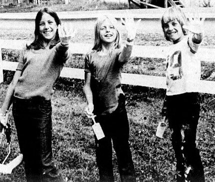 Three children hold up their left hands covered in paint.