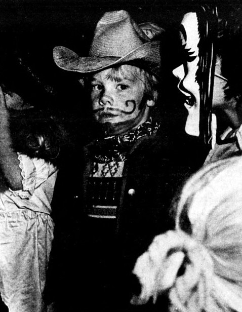 A little boy wears a cowboy costume with a painted mustache.