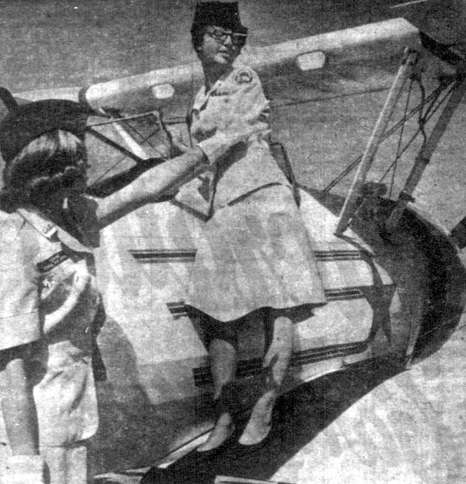 Two young women cadets stand next to a small aircraft.