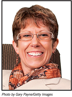 Head shot of Diane Walden, wearing a off while blazer and autumn flower scarf, wearing wire framed glasses.