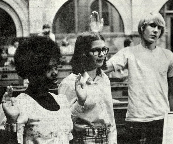 Three high school students hold up their right hands as they take an oath.