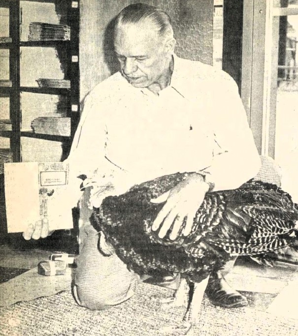 A man holds up a book to a turkey.