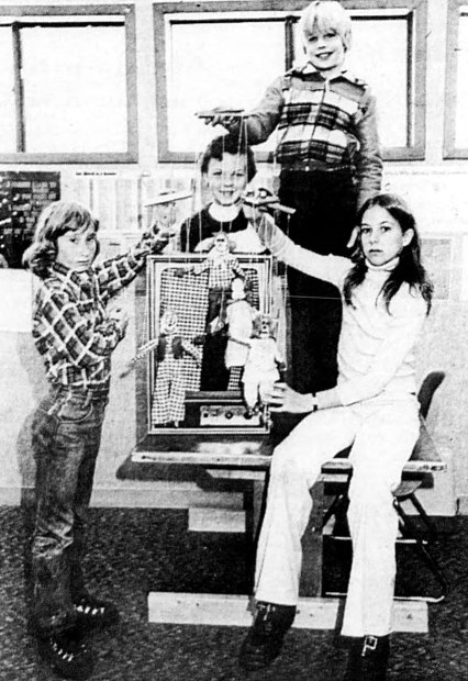 Four children hold up the marionettes they made in school.