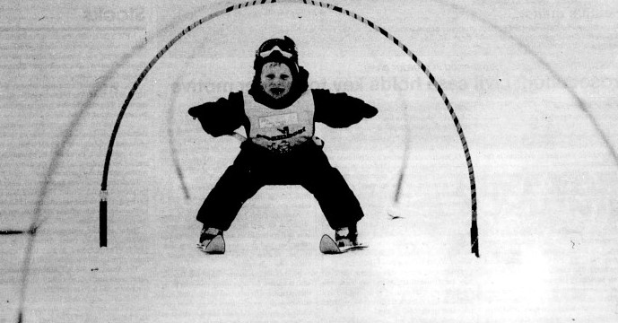 A young child skis under hoops.