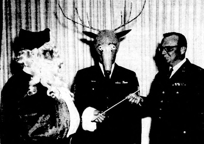 Santa and an Air Force officer hold a baton while another officer dressed as a reindeer looks on.