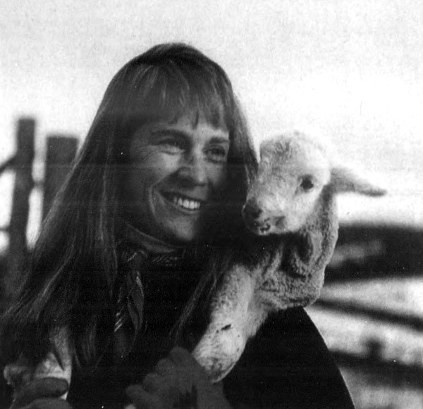 A woman snuggles with a lamb around her neck.