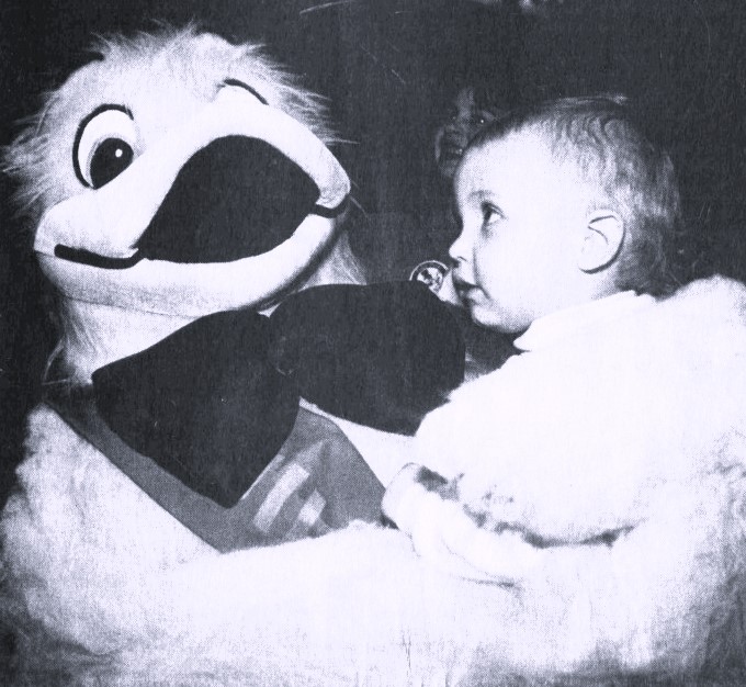 A person in a duck costume holds a baby.