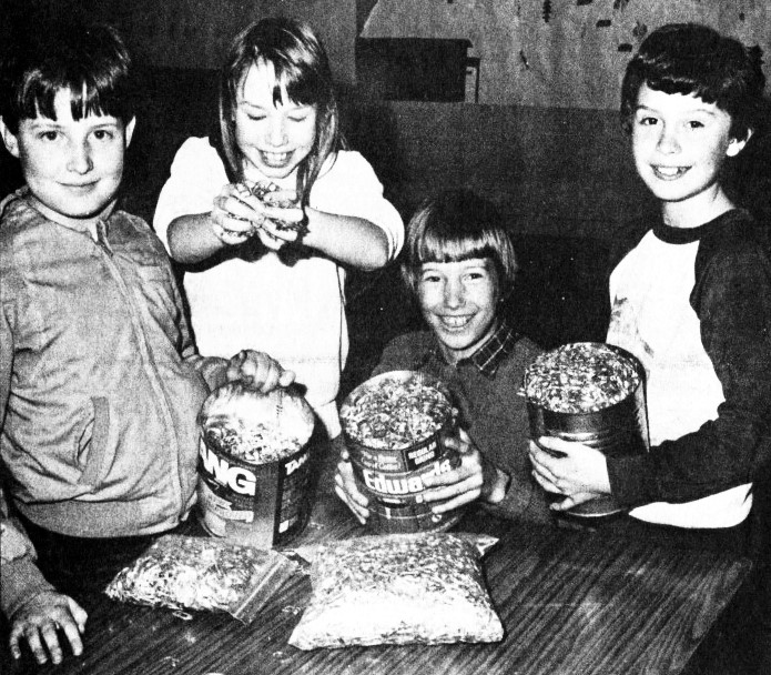 4 children hold several large containers full of pop tops.