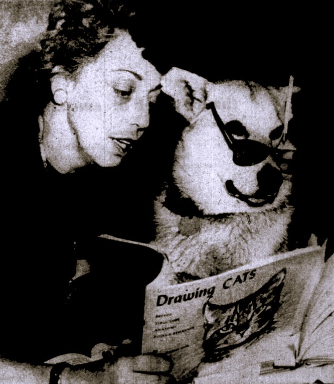 A woman reads from a book called Drawing Cats to a dog wearing glasses.