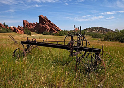 Old and rusting farm equipment sits in a grassy field with sandstone spires in the background.