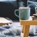 Cup of hot drink on wooden table. Living room interior with blue sofa on background.