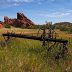 Old and rusting farm equipment sits in a grassy field with sandstone spires in the background.